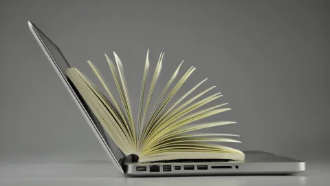 Aufgeklapptes Laptop darauf ein Buch mit aufgefächerten Seiten