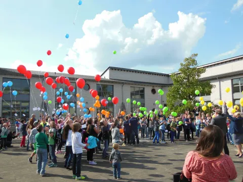 Eine große Gruppe von Schülerinnen und Schülern lässt Luftballons aufsteigen