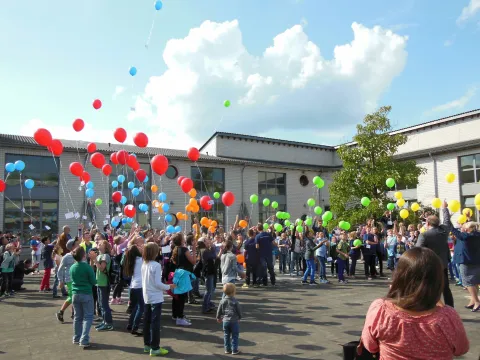 Eine große Gruppe von Schülerinnen und Schülern lässt Luftballons aufsteigen