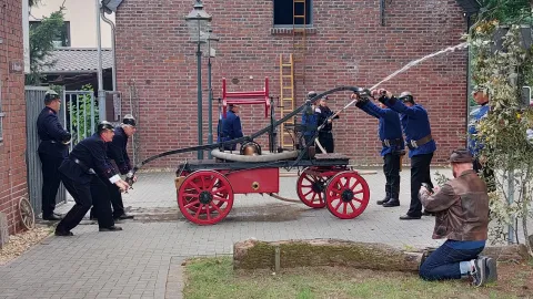 Eine Gruppe von Männern löscht einen Brand mit einer historischen Löschspritze