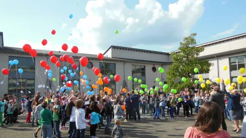 Eine große Gruppe von Schülerinnen und Schülern lässt Luftballons aufsteigen