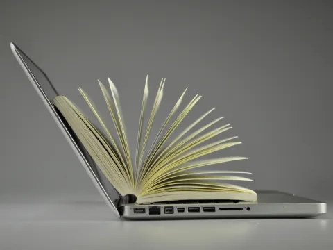 Aufgeklapptes Laptop darauf ein Buch mit aufgefächerten Seiten
