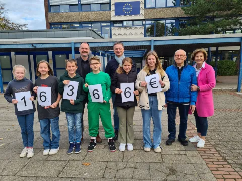 Schüler mit Zahlenkarten flankiert von Erwachsenen auf Schulhof 